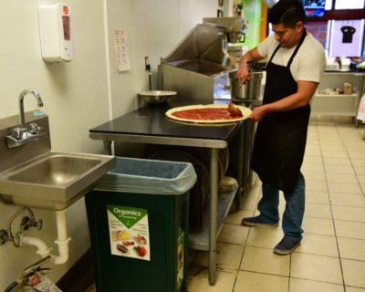Man making a pizza next to organics recycling bin