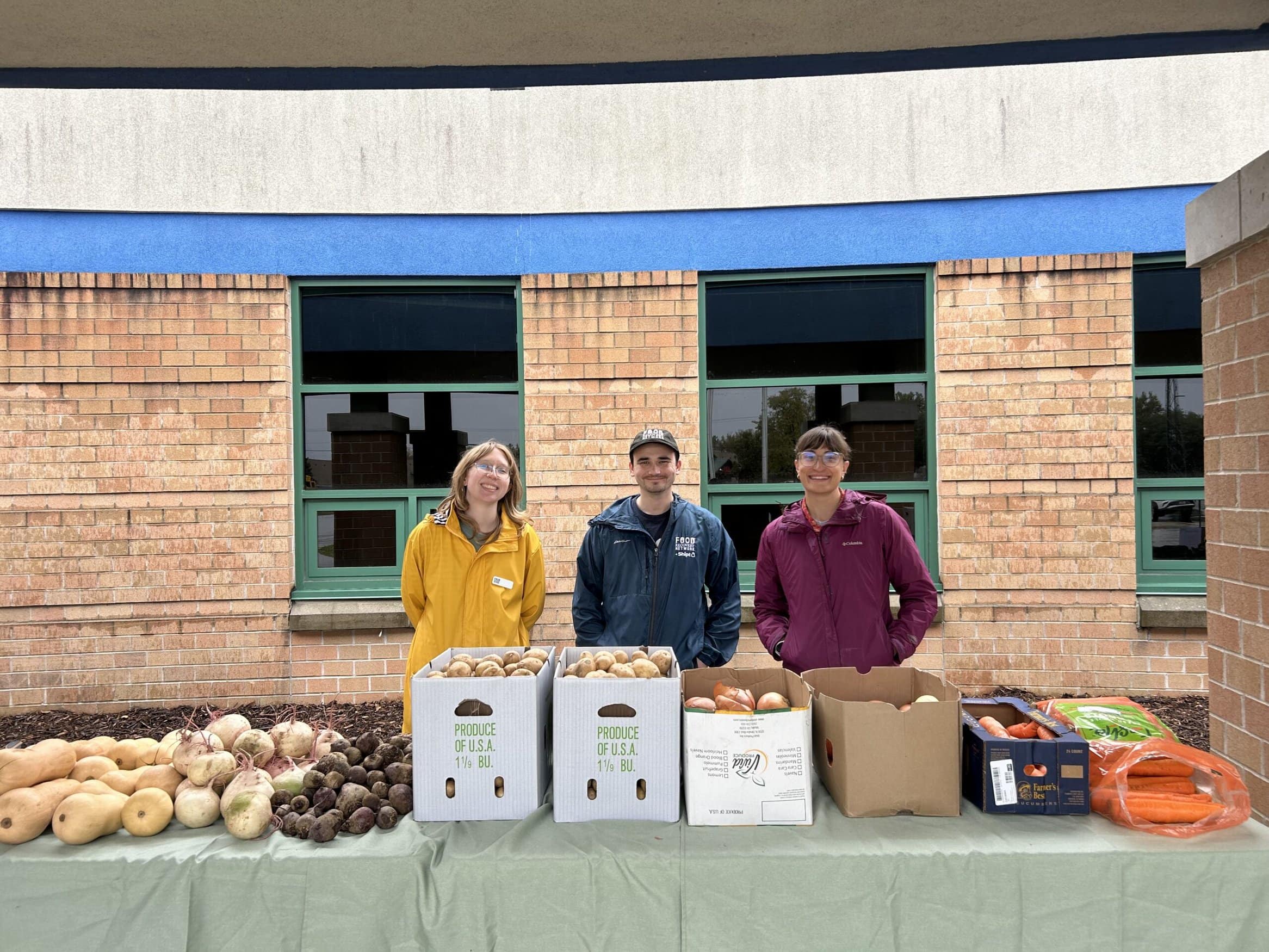 Three people smiling behind a table with produce on it