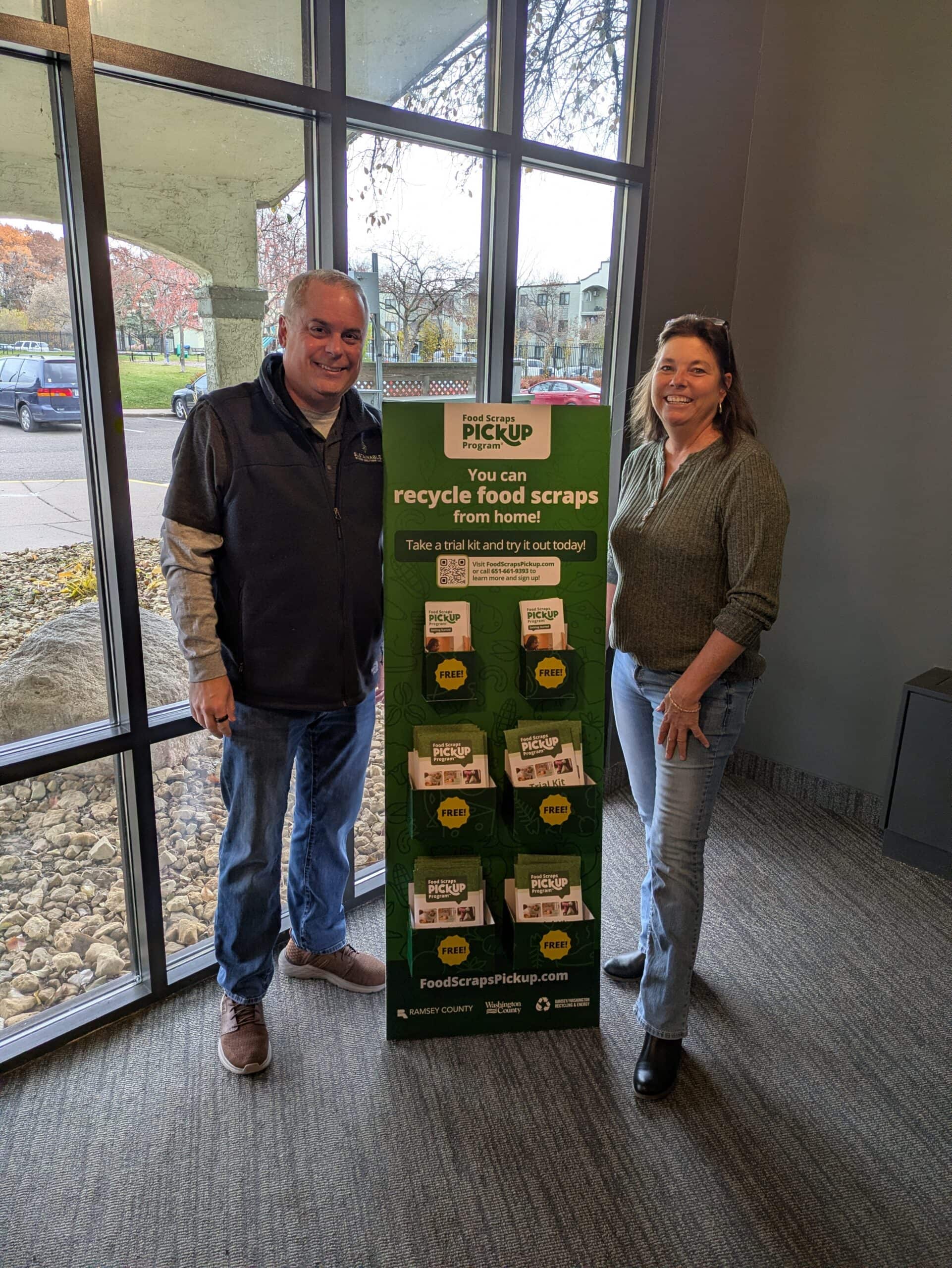 Photo of two people standing next to promotional material for the Food Scraps Pickup Program