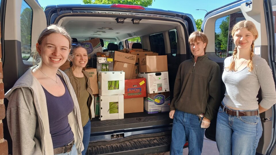 Group of people smiling in front of a car with an open trunk with boxes of food in it