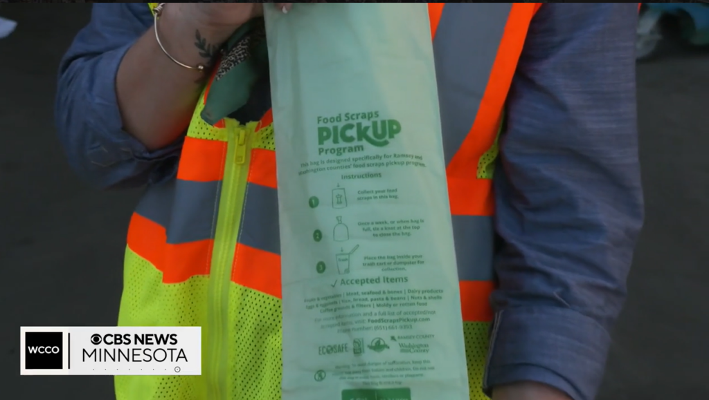 Screenshot of the news video of a person wearing a high-vis vest holding a Food Scraps Pickup Program bag
